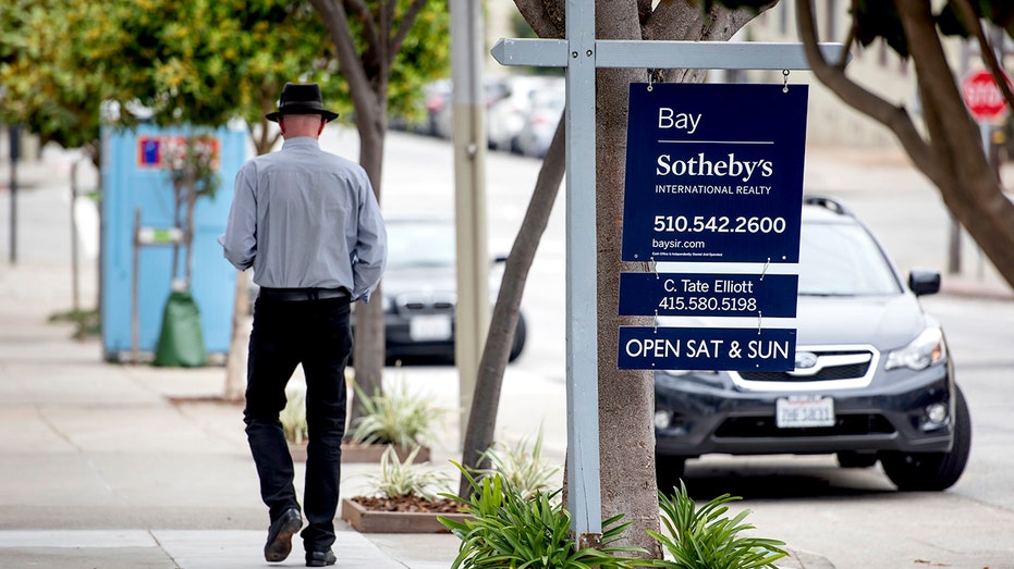 A man walks past a "For Sale" sign for a house in San Francisco, California.