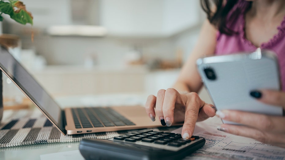 A woman is at home, holding a collection of paper bills and financial plans. She appears to be focused on managing her personal finances, possibly sorting through bills, budgeting, or organizing her financial matters.