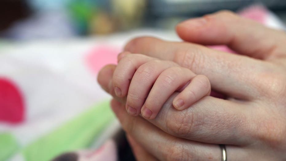 A photo of a newborn baby holding an adult hand